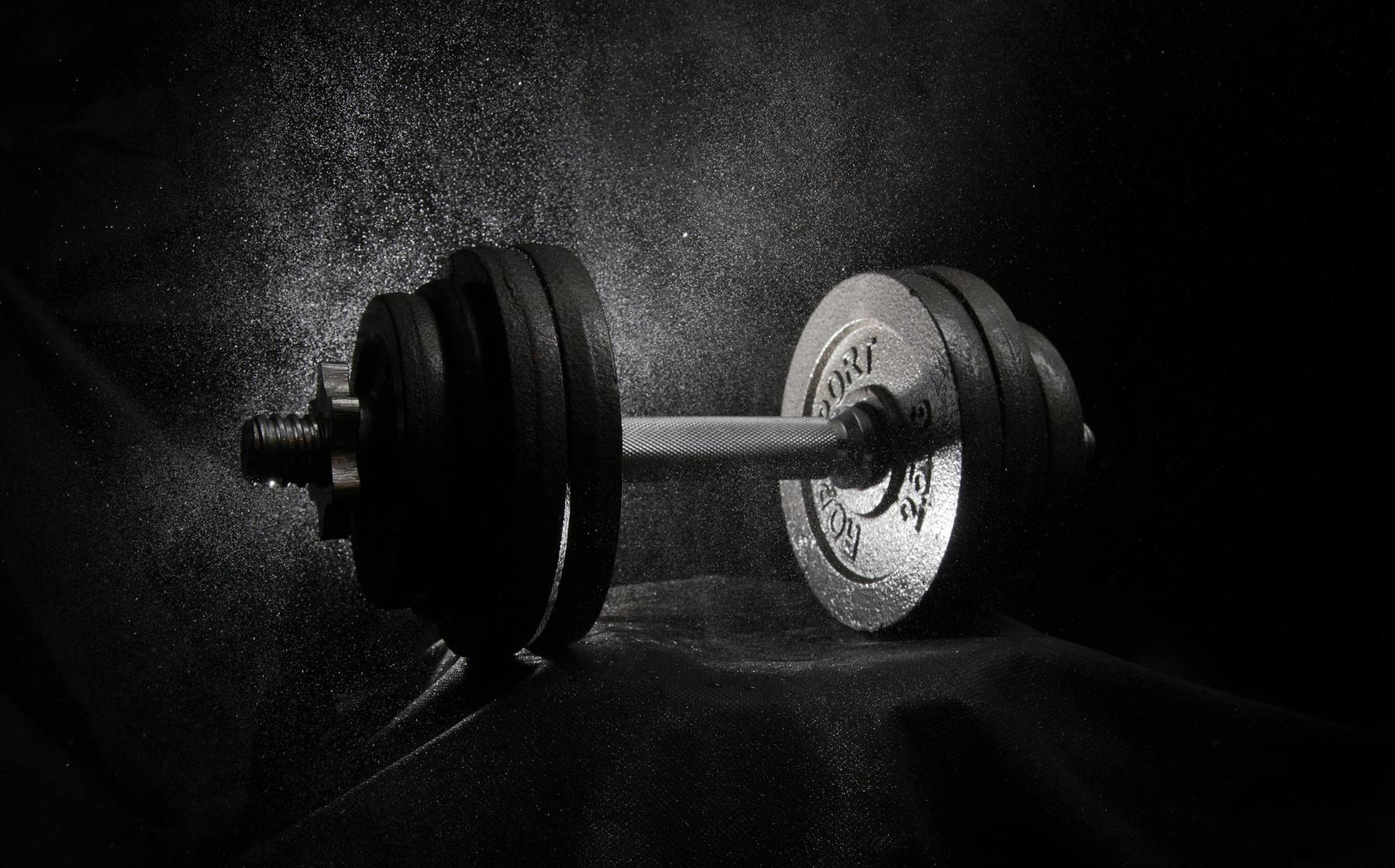 Barbell in a cloud of chalk dust against black